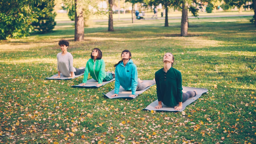 Attractive girls in trendy sportswear are doing succession of yoga exercises on mats in park on warm autumn day. Wellness, active lifestyle and relaxing young people concept.