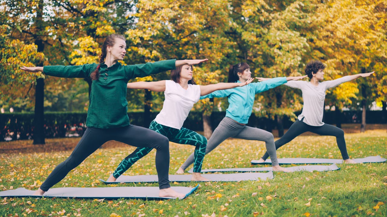 Four women practicing yoga in a park surrounded by autumn foliage.