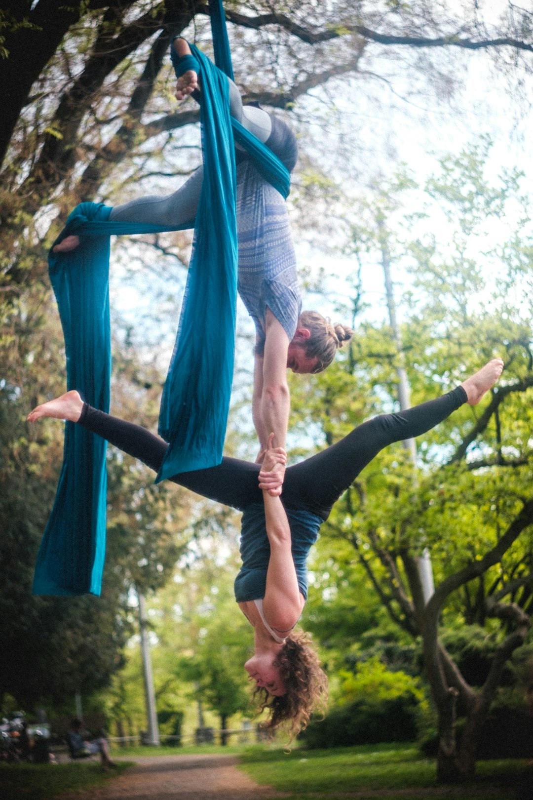 a couple doing aerial silk flying yoga outdoor in the nature park during daytime